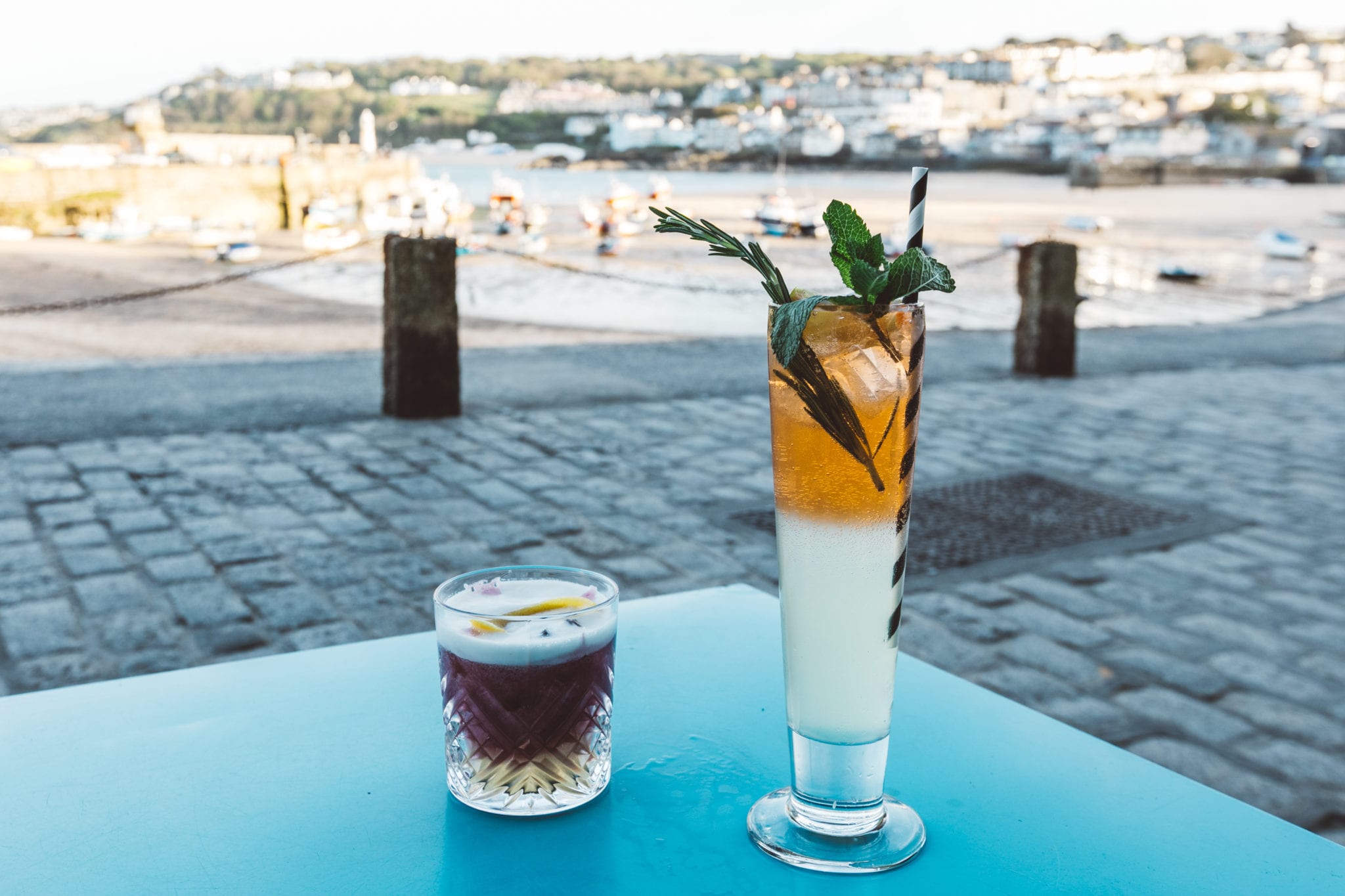 Two cocktails on a blue table overlooking St Ives harbour