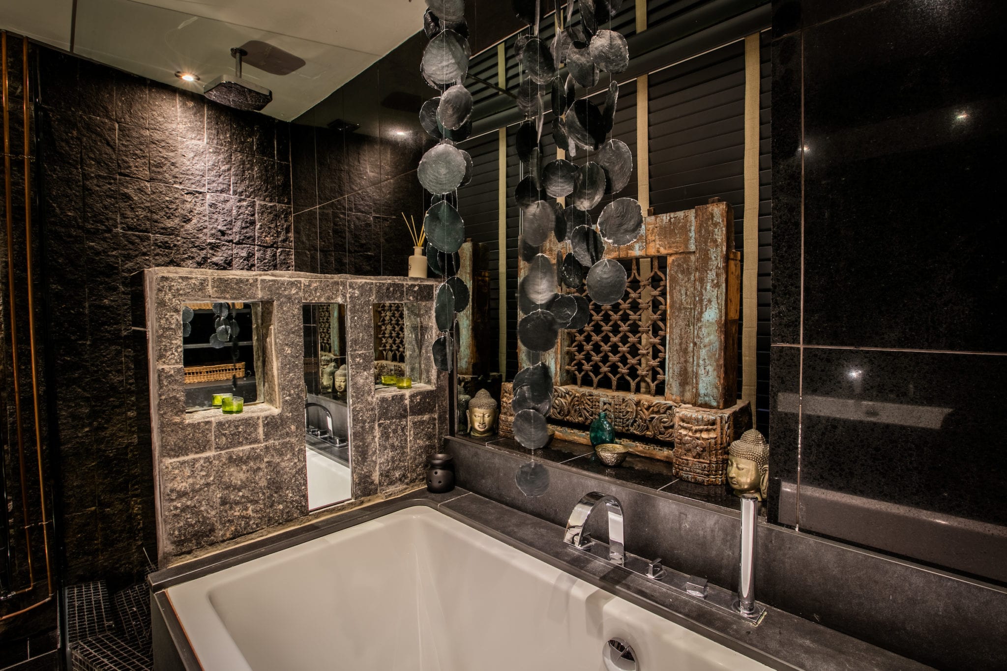 A bathroom with black slate, exposed stone and luxurious ethnic art