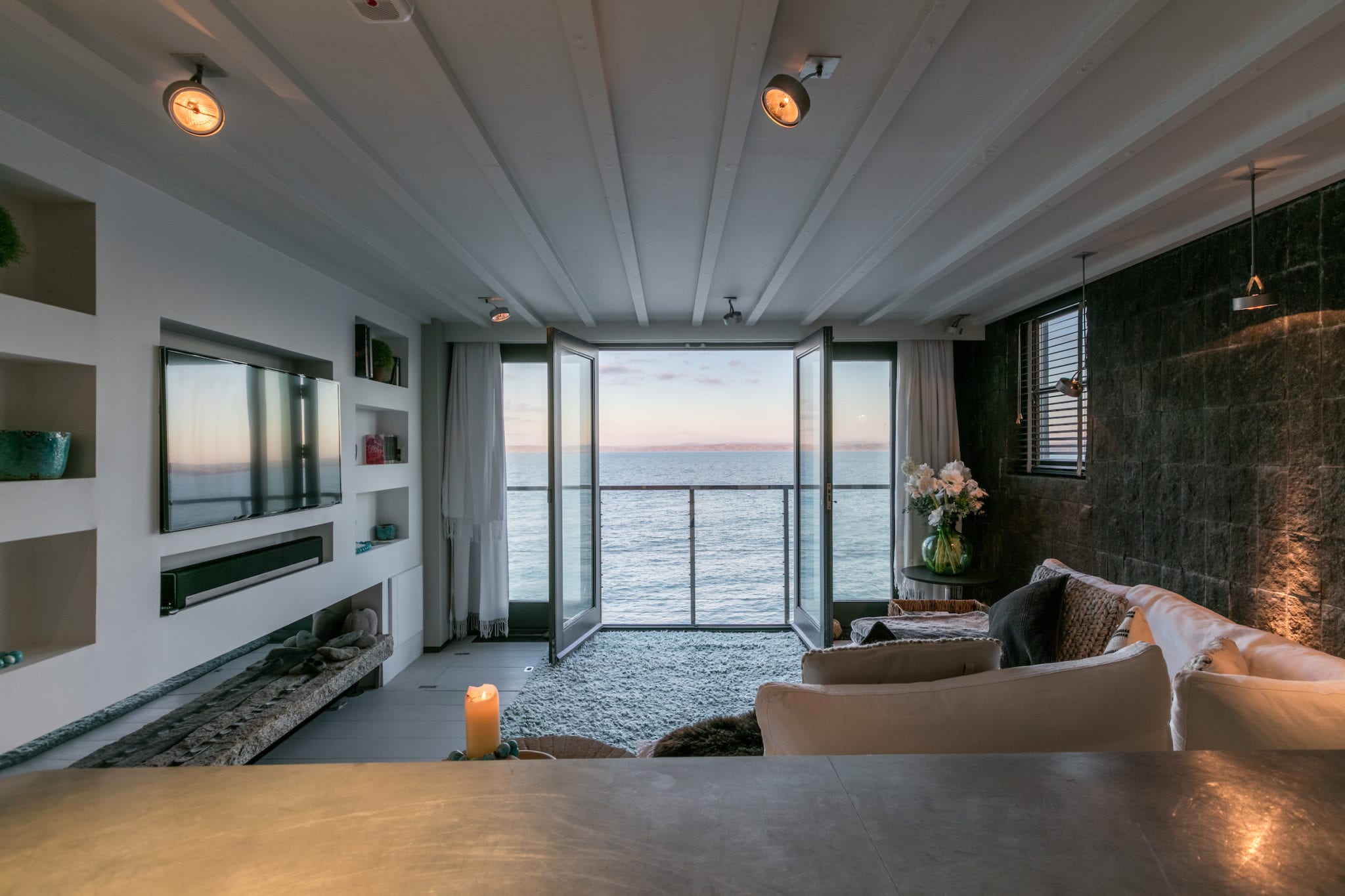 Black Moon's warmly lit living room with sea views, a large sofa and a flat screen TV built into the wall