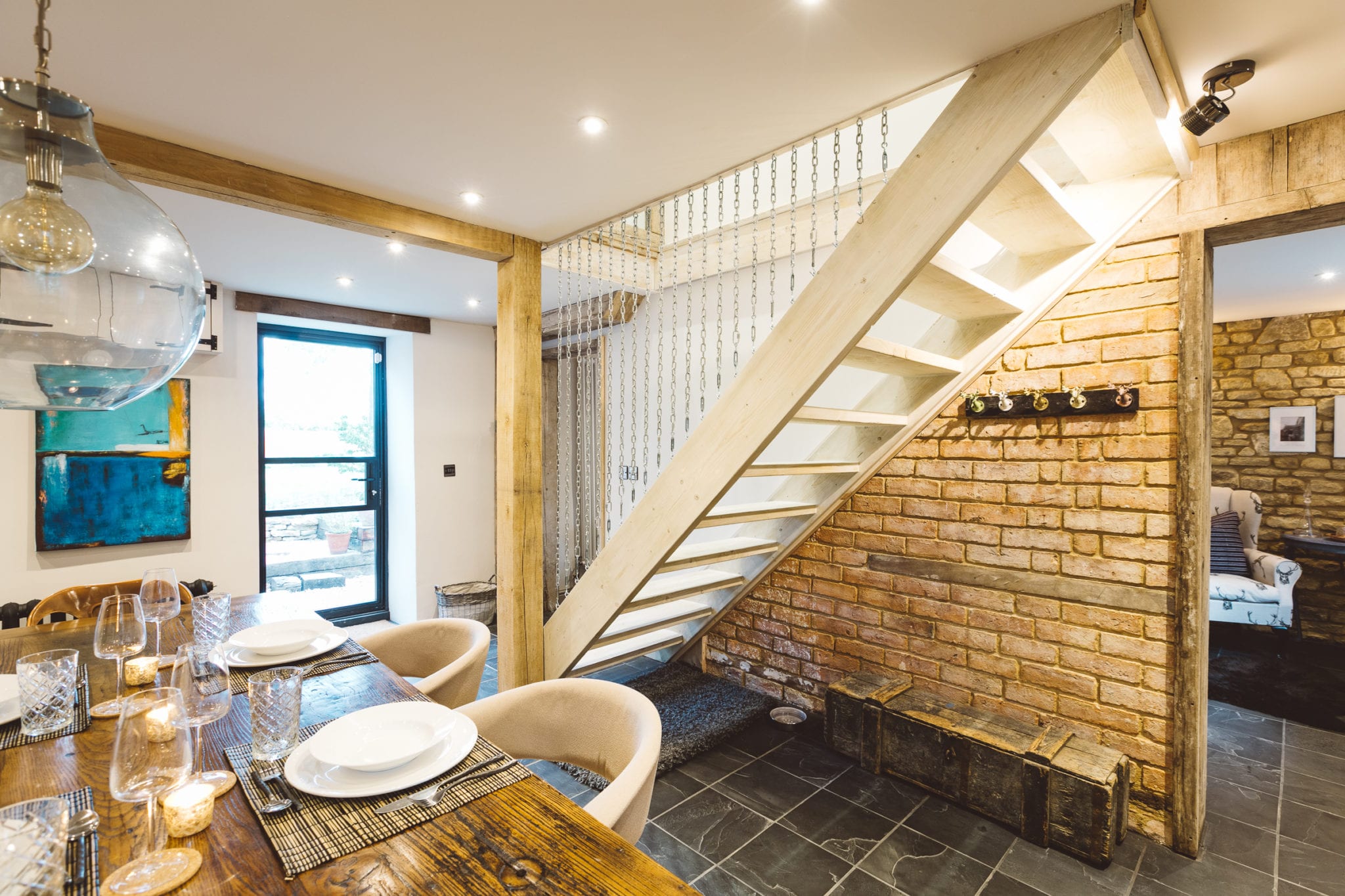 An open plan cottage interior with a floating staircase with chain rails