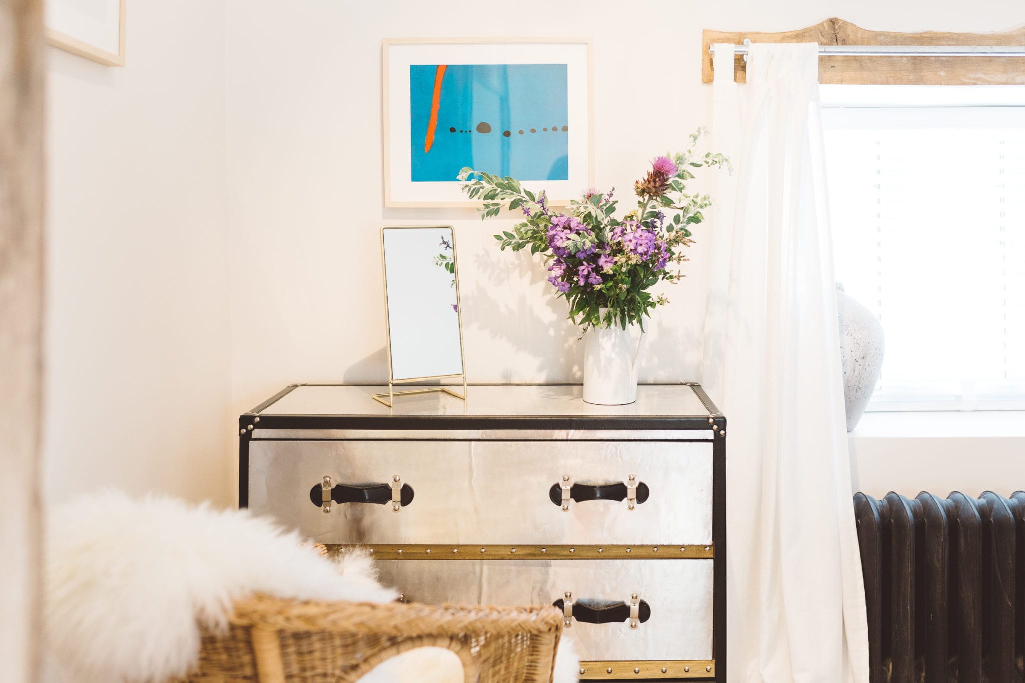 A silver chest of drawers with a small mirror and a vase of flowers on it