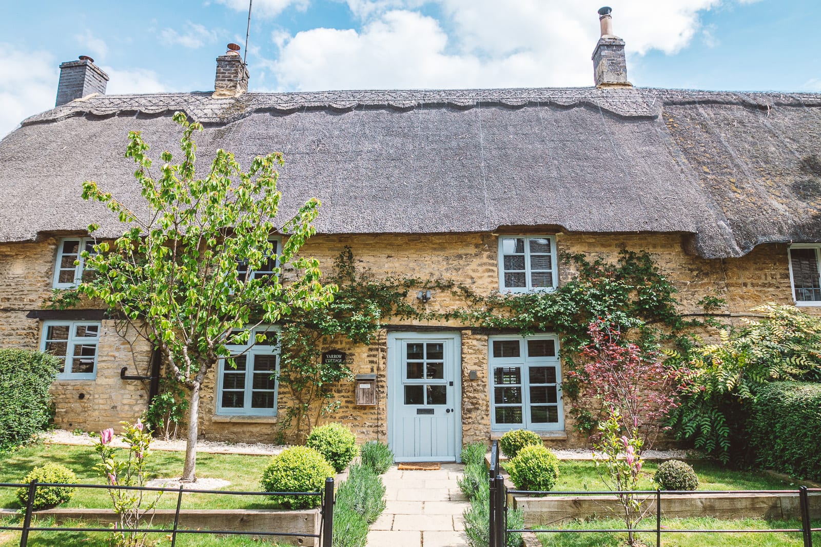 The exterior of a country cottage with a large thatched roof and a lovely front garden