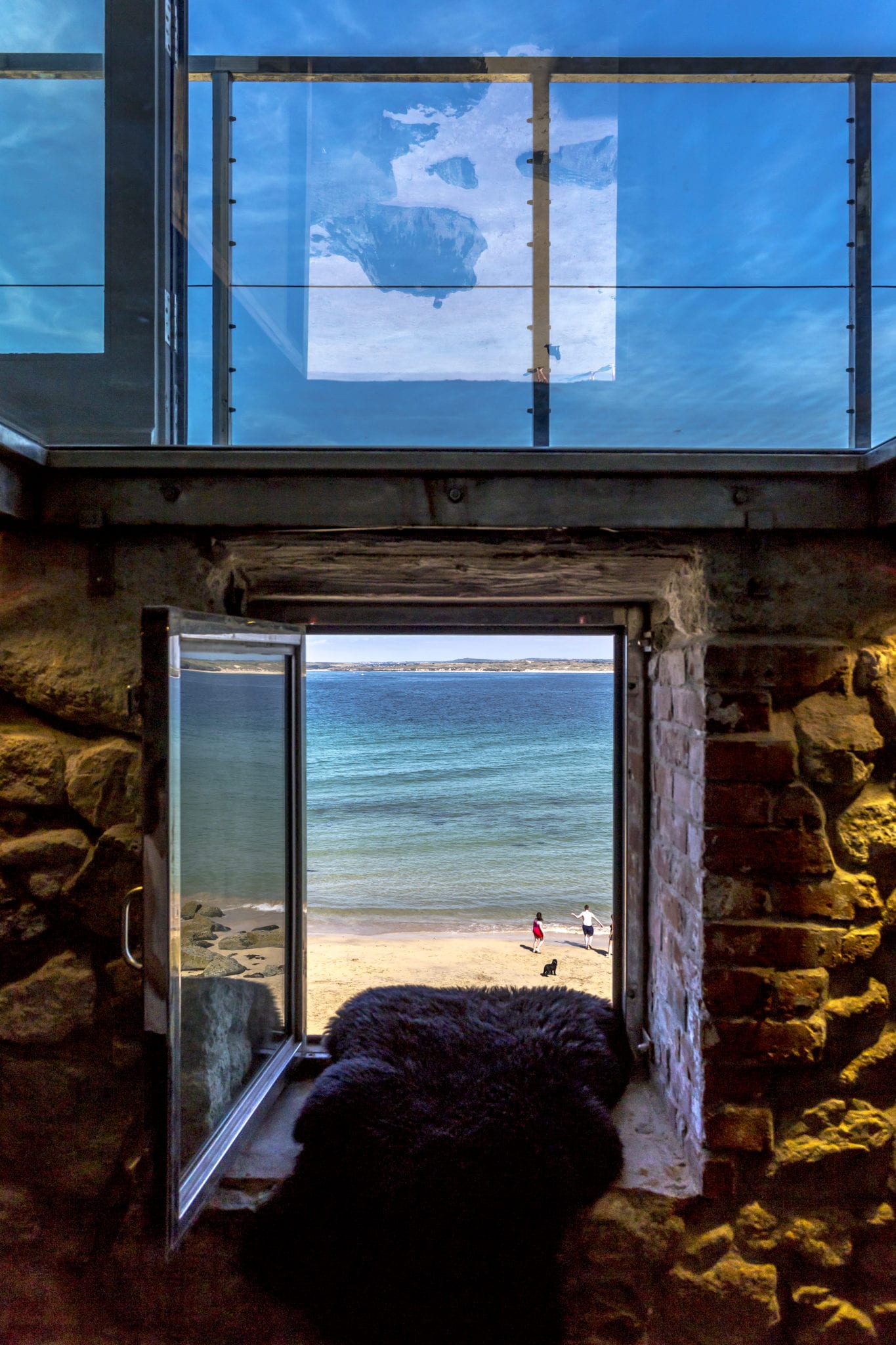 A small window built into a stone wall revealing a beach and a seafront views