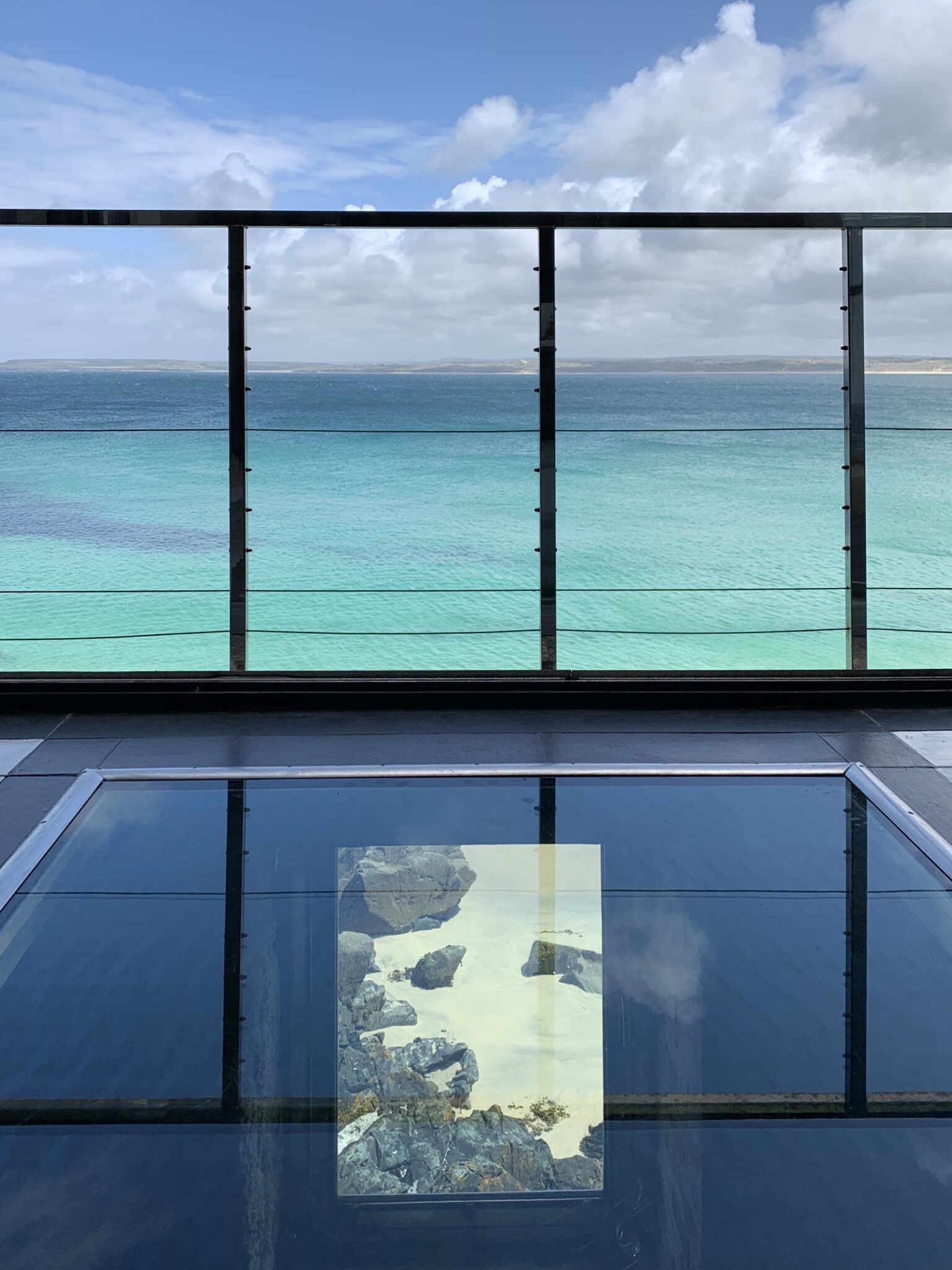 An apartment with a glass floor and a balcony overlooking the bright blue sea