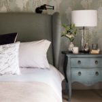 Detail of bedroom with patterned grapevine wallpaper and a side table with a lamp and flowers