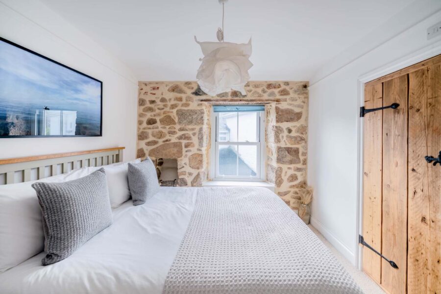 Room with window and double bed with grey pillows and throw