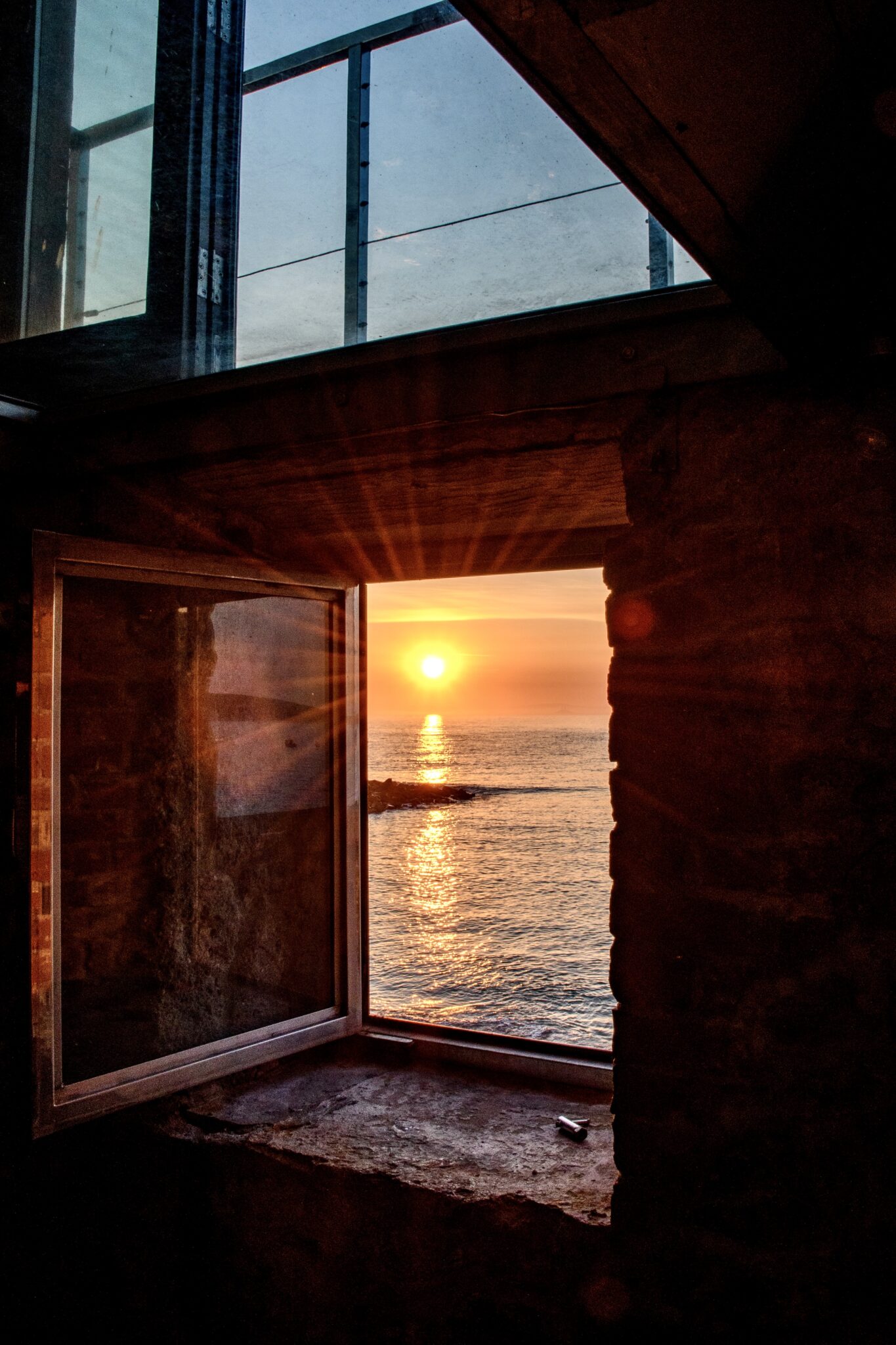 A small window in a stone wall with a view of the sunrise over the sea