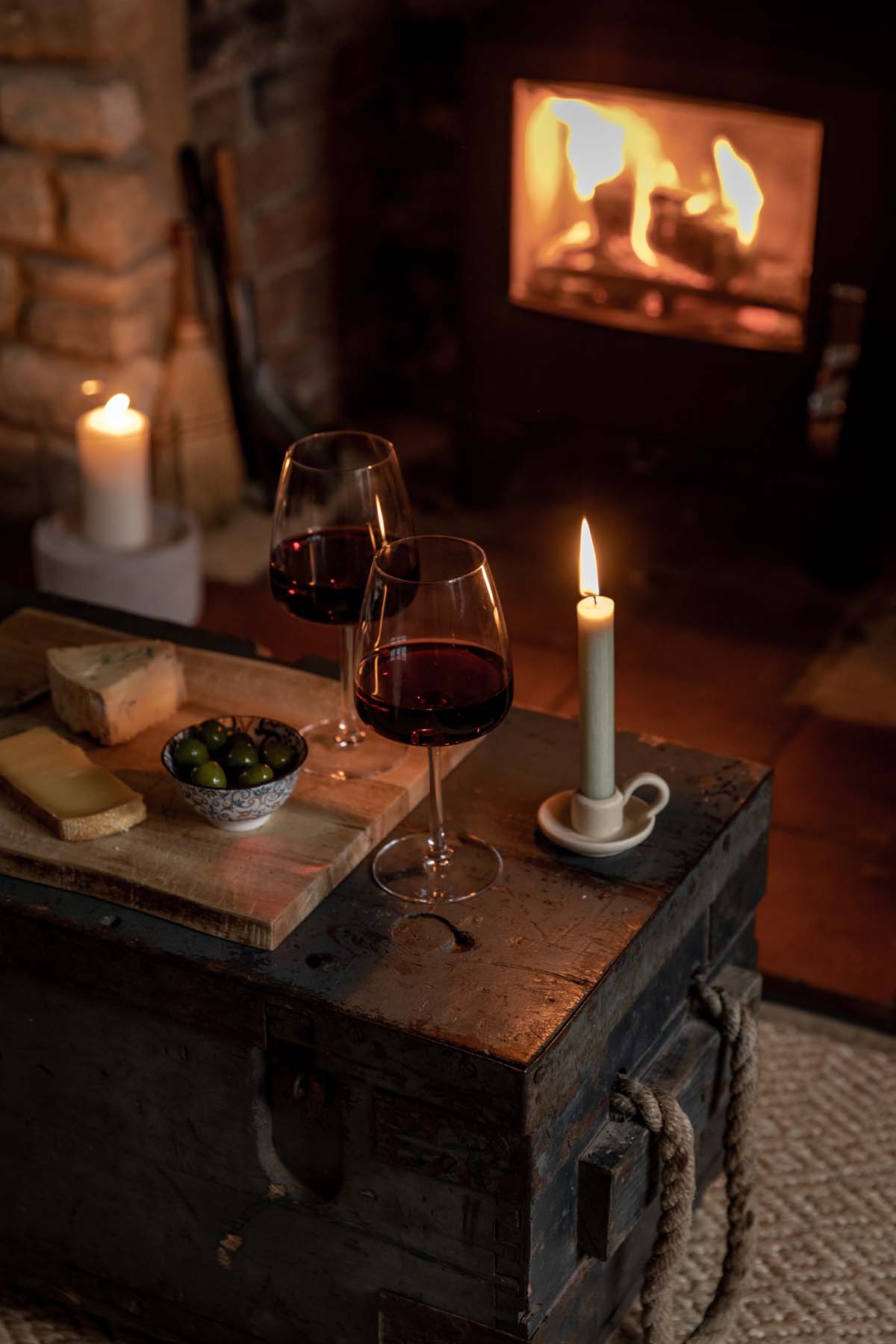 Two glasses of red wine and a candle by the fireplace