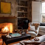 Living room with a velvet sofa, wallpaper, roaring fire and plantation shutters