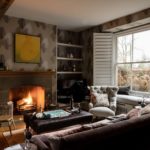Roaring fireplace in a modern country house living room with a large bay window and plantation shutters