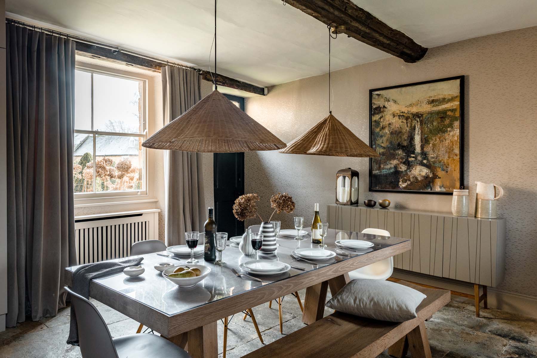 Dining table oak beams, hanging rattan lampshades, artwork and modern chairs