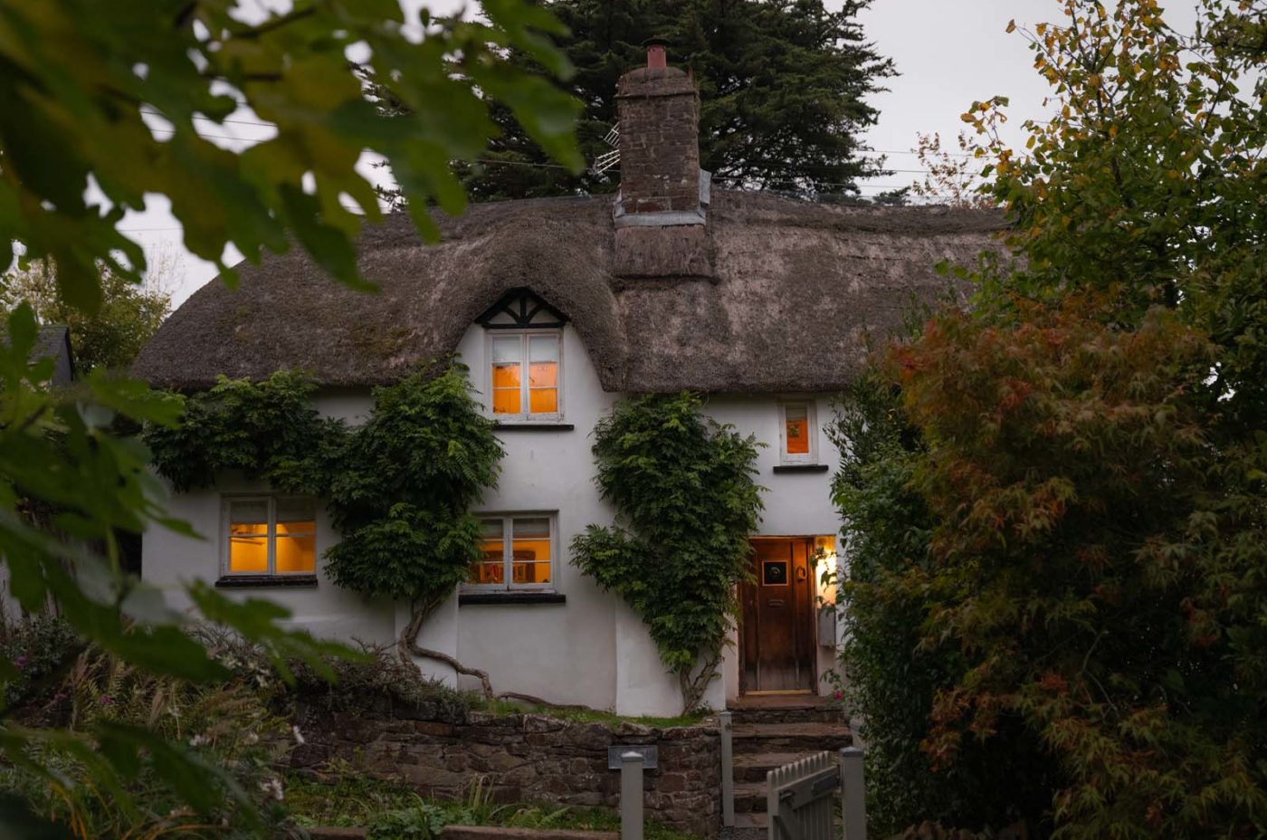 Thatched Cottage Exterior at dusk surrounded by leaves