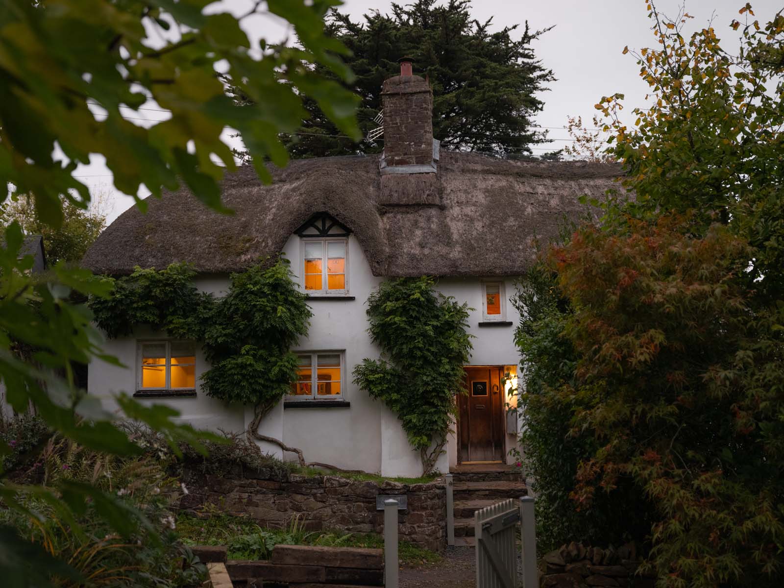 Thatched Cottage Exterior at dusk surrounded by leaves