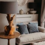 Driftwood lamp on a wooden table by a seating area with grey modern sofa and blue velvet cushions