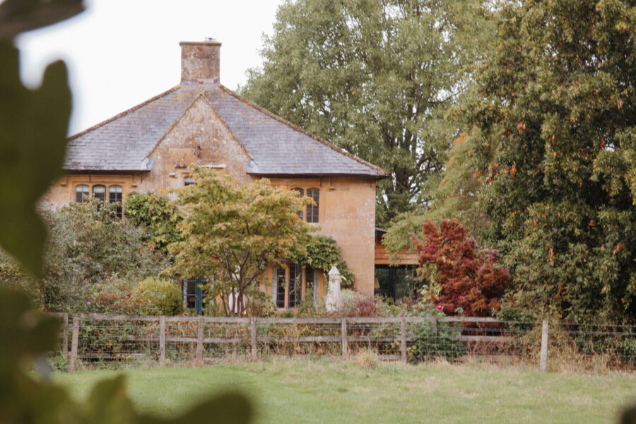 A beautiful country house surrounded by trees and a. fence by a field