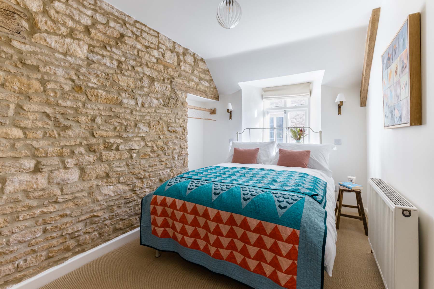 Double bedroom with colourful quilt and exposed brick wall