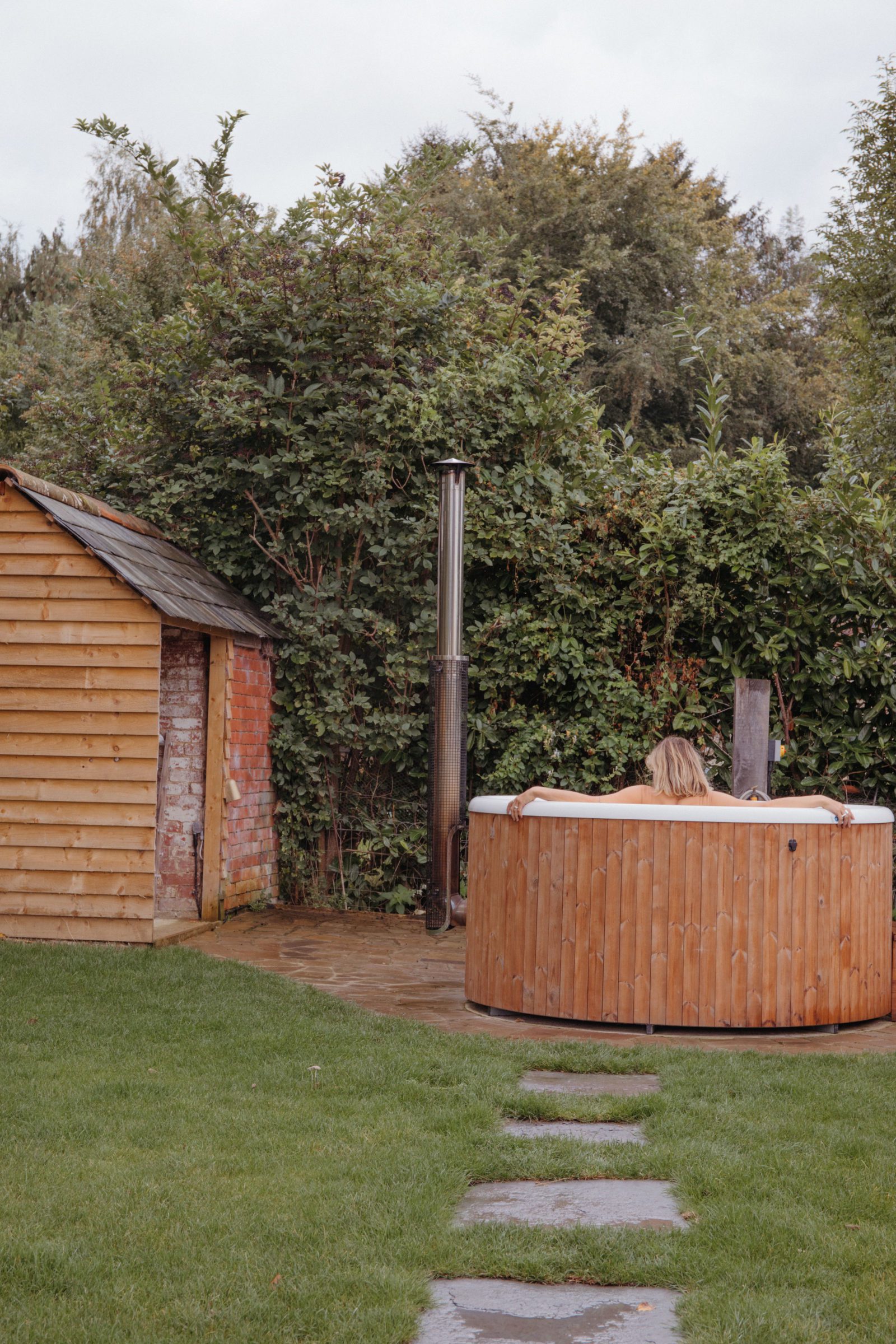 A woman in a wooden hot tub in a garden