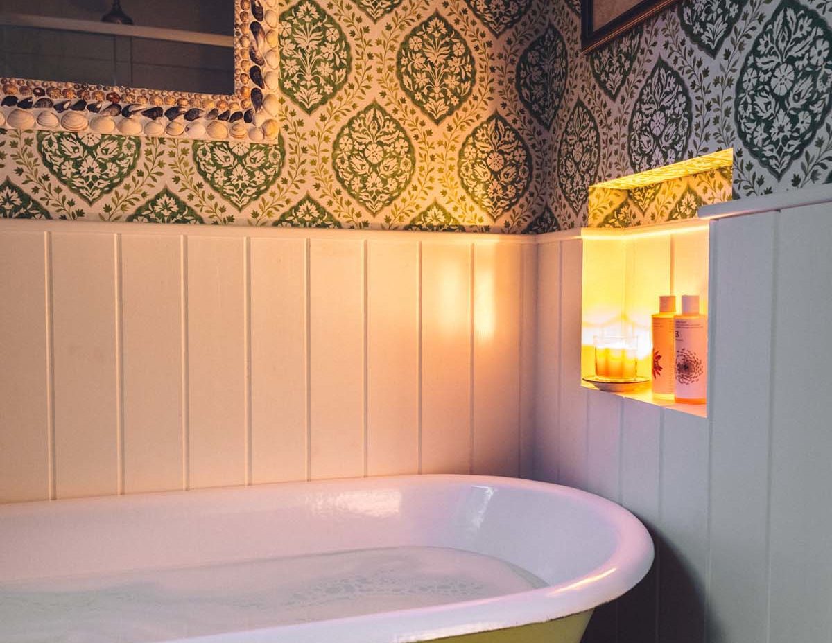 Cosy candlelit cottage bathroom with a green roll top tub