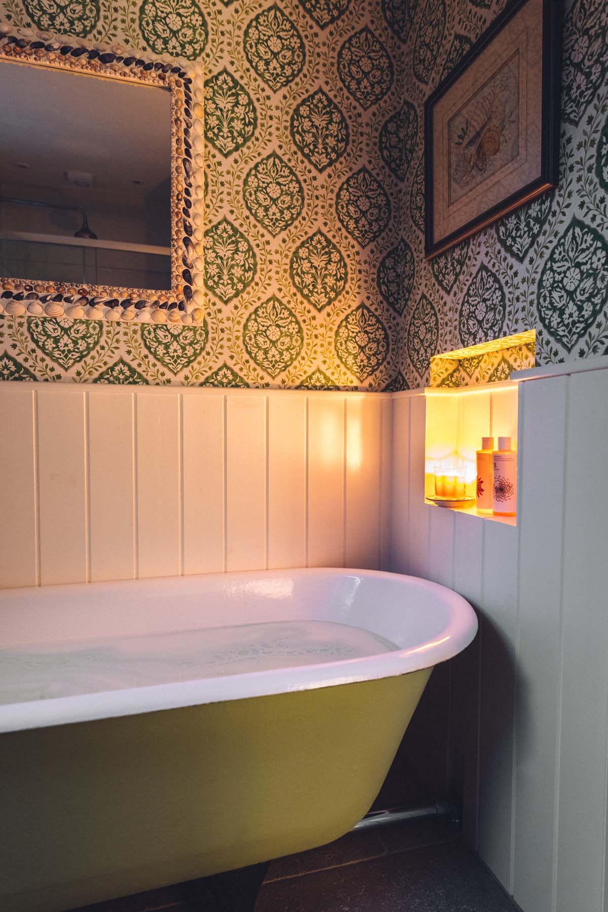 Cosy candlelit cottage bathroom with a green roll top tub