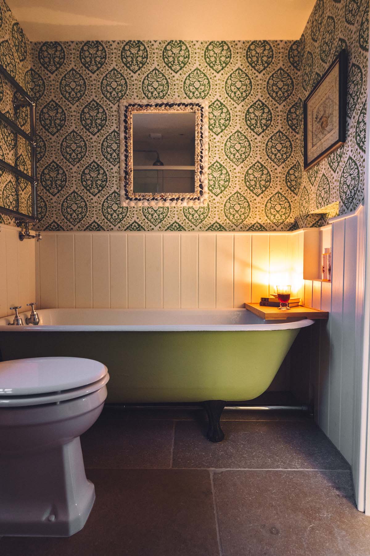 Cosy candlelit cottage bathroom with a green roll top tub