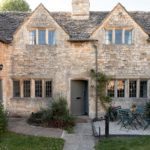 Honey coloured Cotswolds stone cottage with stylish grey painted door and courtyard front garden