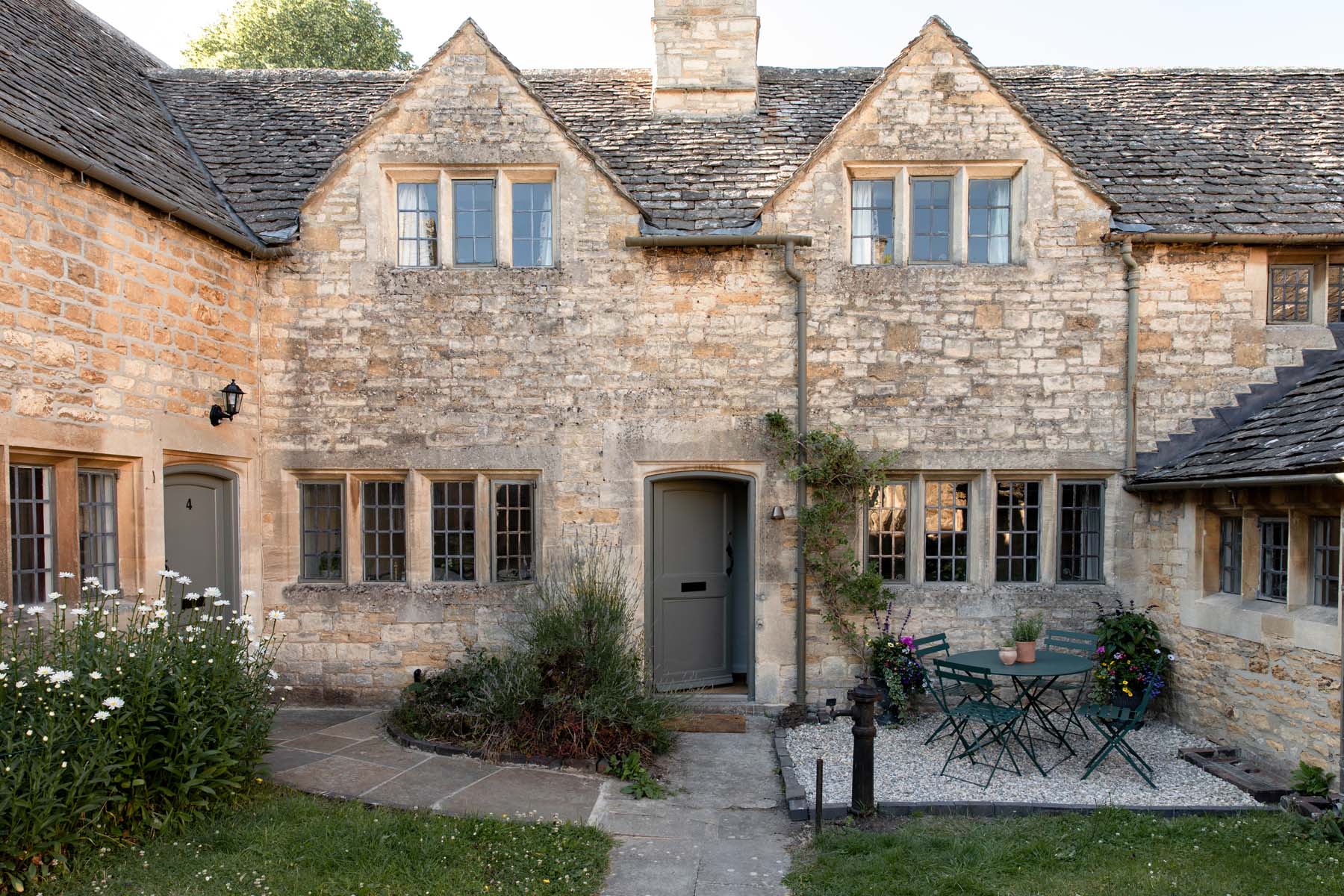 Honey coloured Cotswolds stone cottage with stylish grey painted door and courtyard front garden