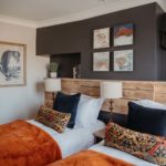 Twin bedroom with orange velvet throws with wood cladding