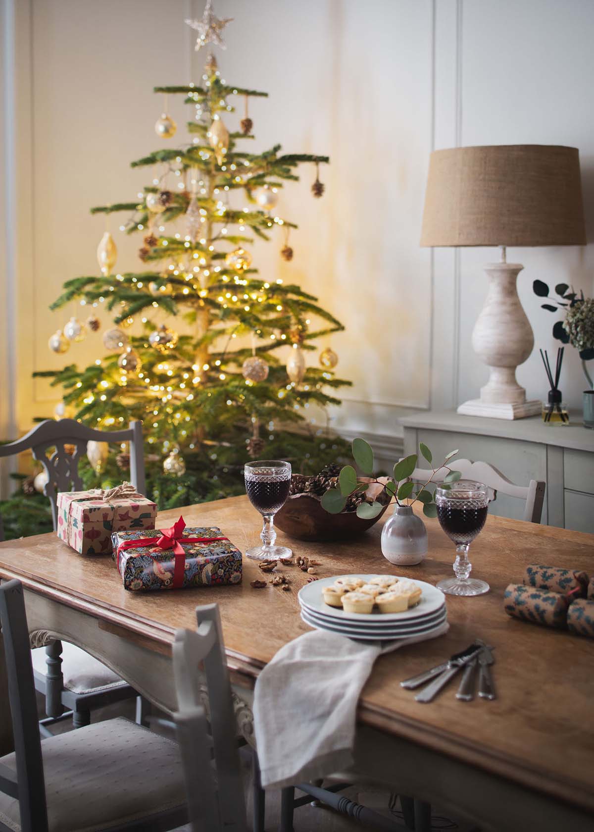 lights on Christmas tree by with presents and wine on table