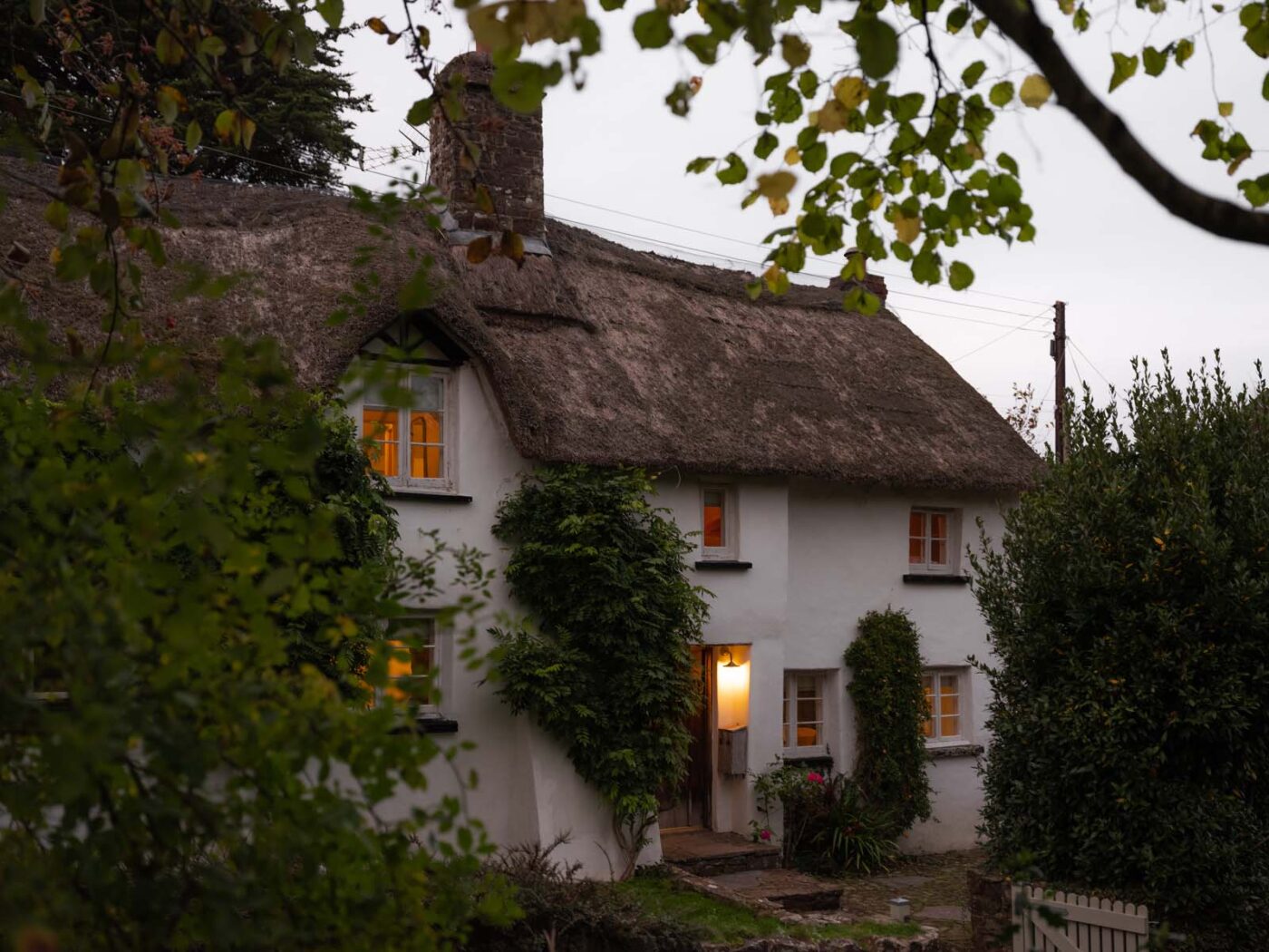 A cosy thatched cottage at dusk with lights on inside