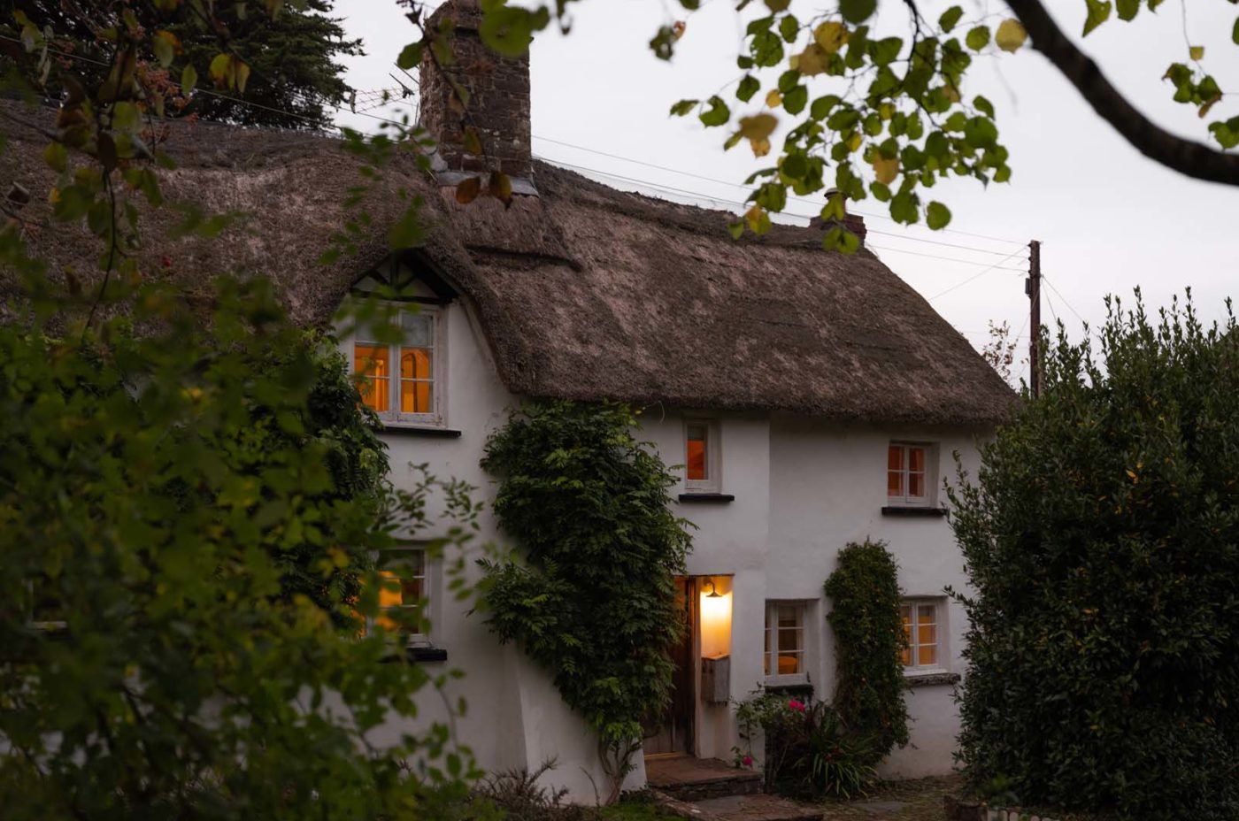 A cosy thatched cottage at dusk with lights on inside