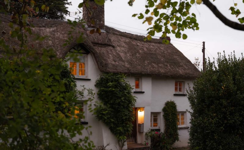 A cosy thatched cottage at dusk with lights on inside
