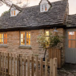 Honey coloured stone cottage with a wooden fence