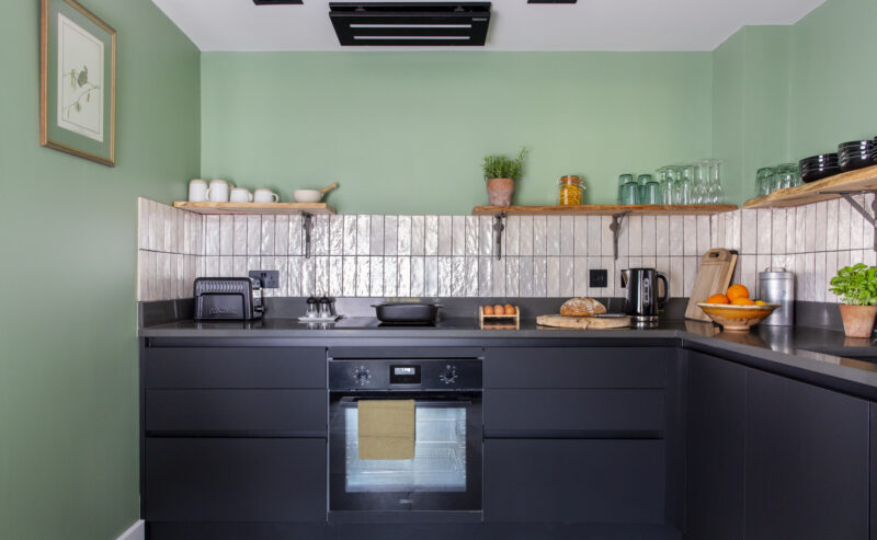Modern kitchen with black units, white tiles, expose shelves and green walls