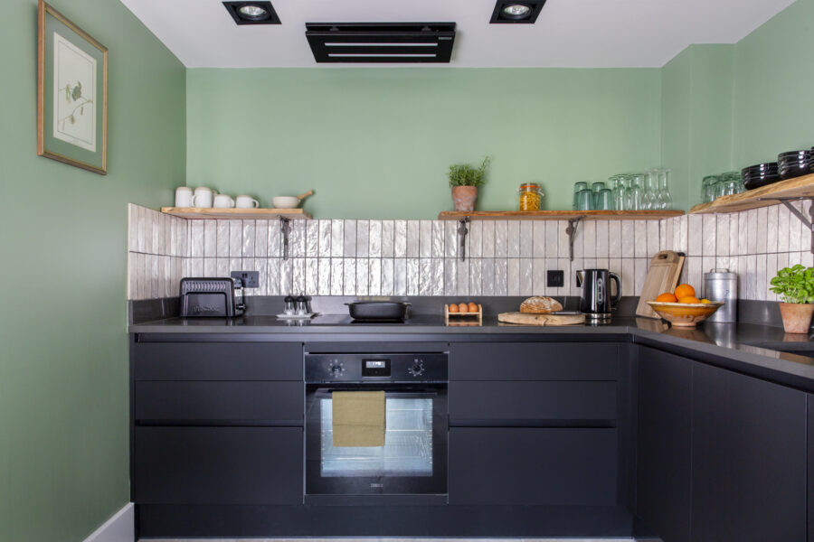 Modern kitchen with black units, white tiles, expose shelves and green walls