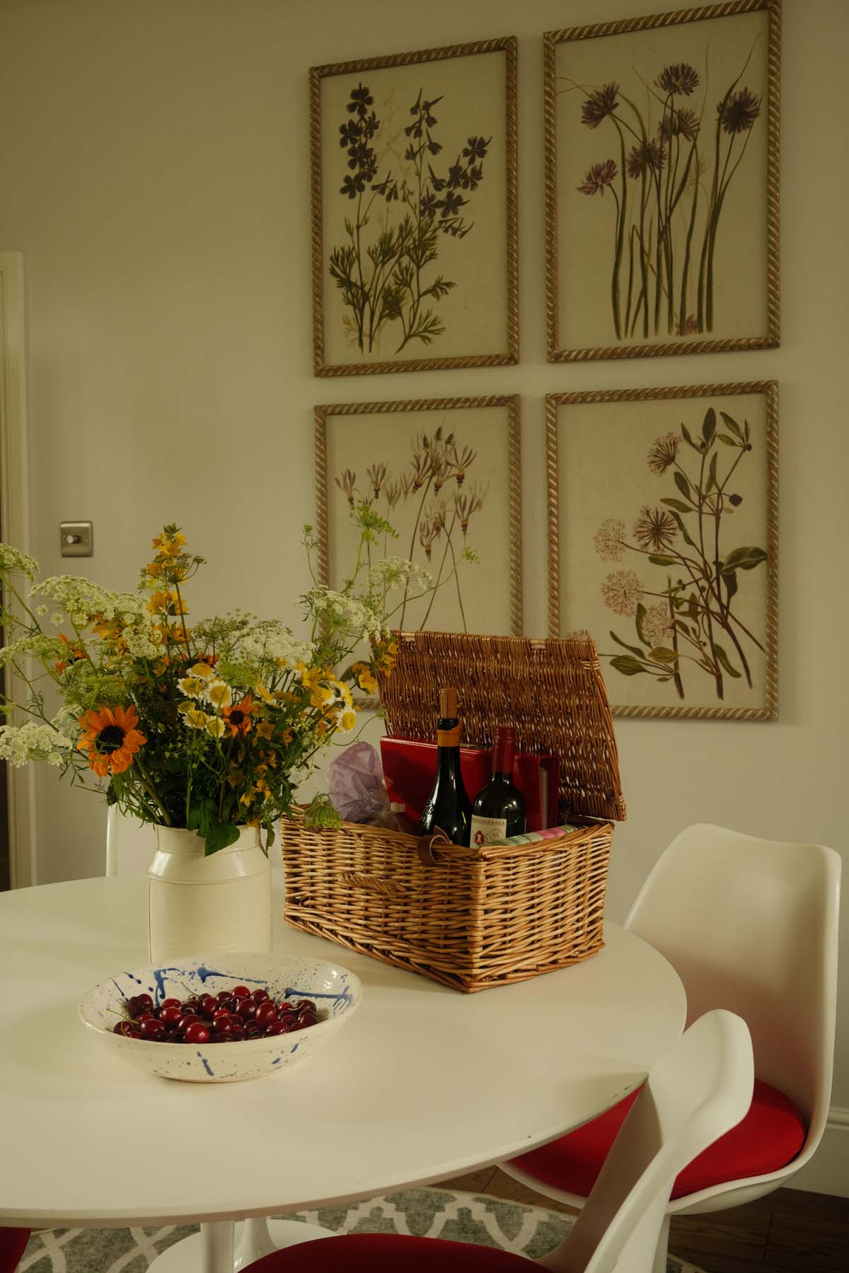flowers on table next to picnic hamper with botanical prints on the wall in the background