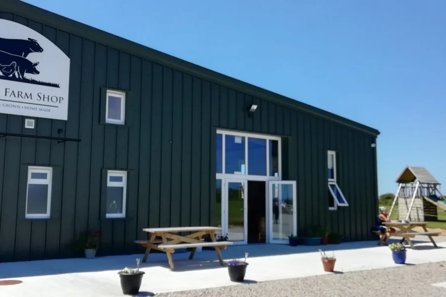 An industrial farm shop front with benches in foreground and blue skies in the background.