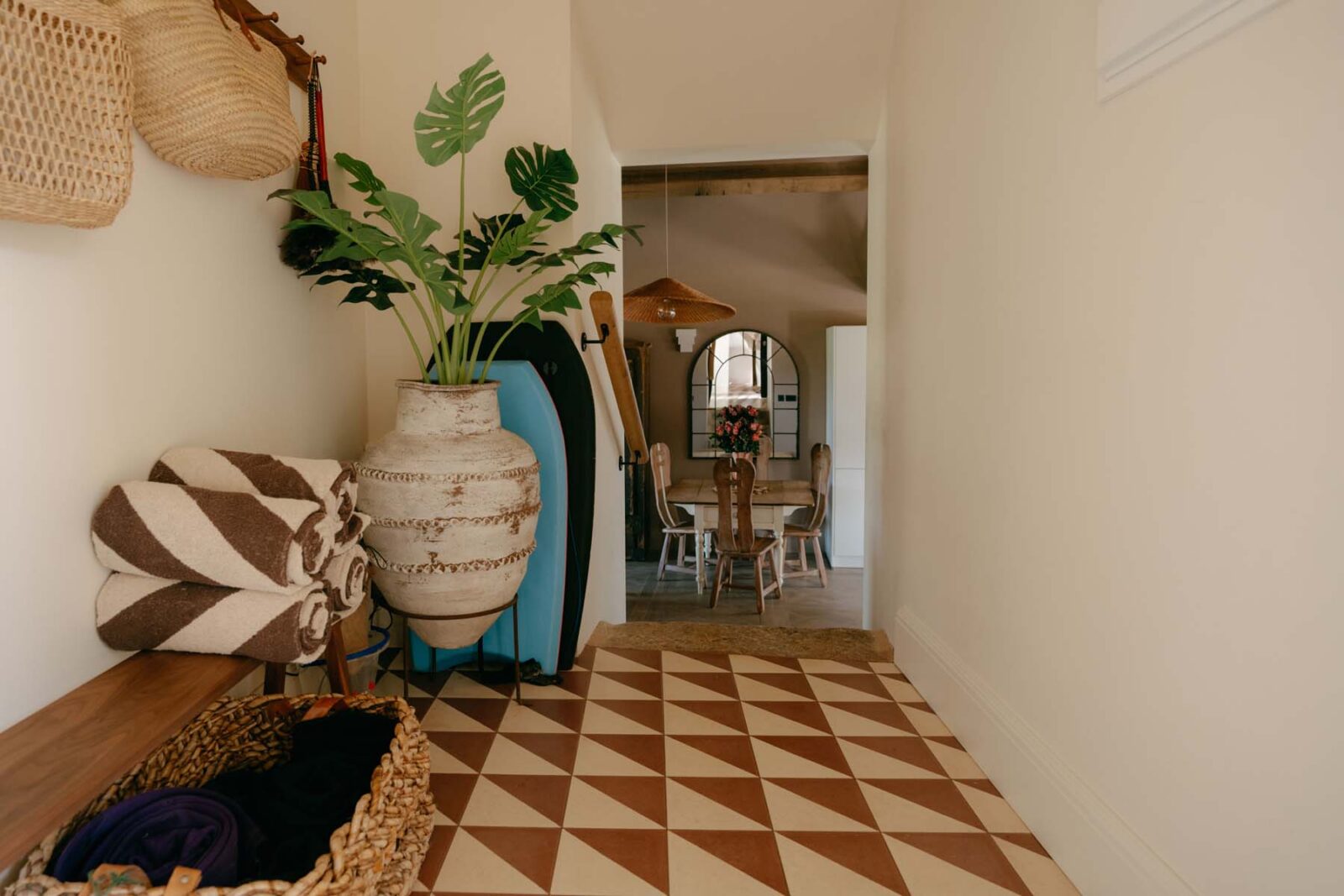 A hallway with geometric floor tiles, matching towels rolled up in the corner and a green pot plant.