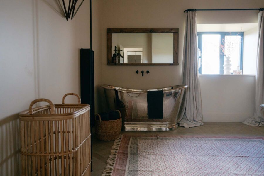 A silver freestanding bathtub in the corner of a room with a mirror on the wall behind it.