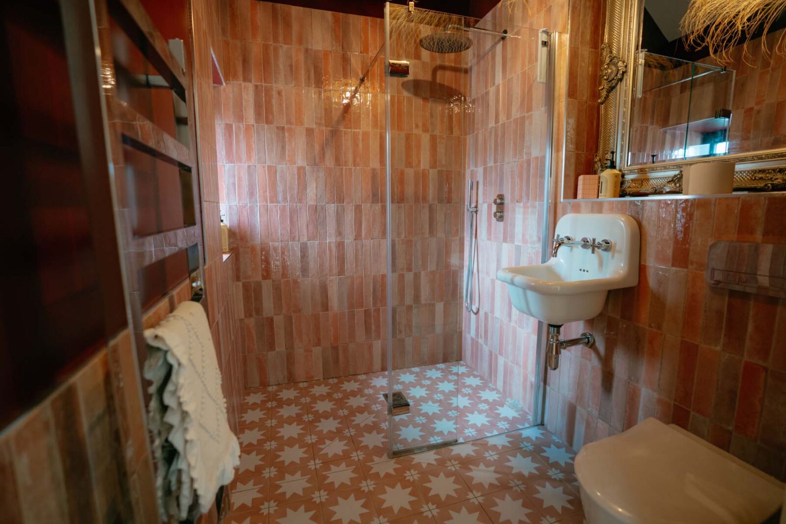 An empty shower next to a basin with pink bathroom tiling.