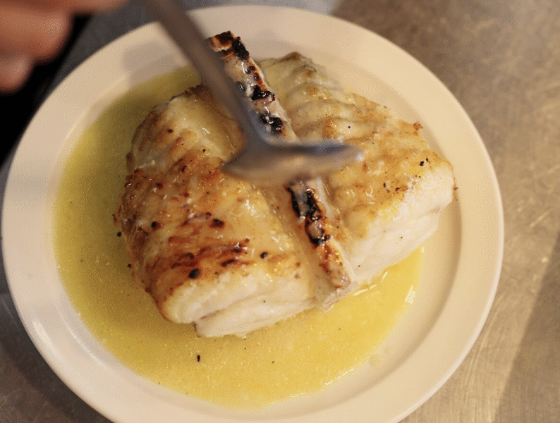 A spoon tucking in to a plate of buttery white fish.