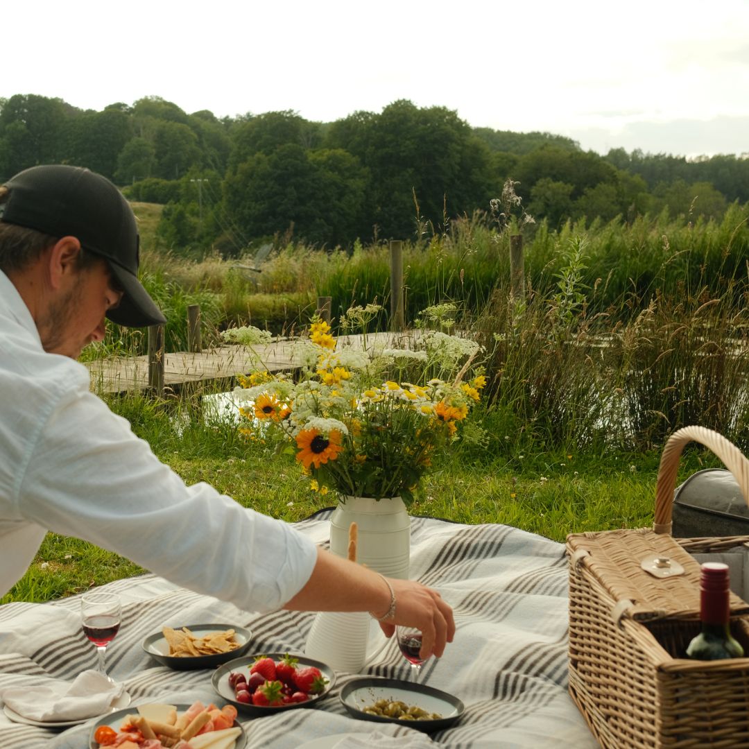 A picnic blanket and flowers are laid out in front of a lake.