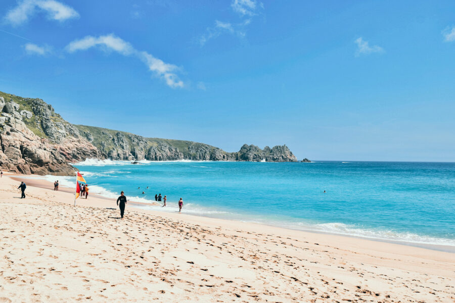 Sandy beach with bright blue sea and cliffs in the background.