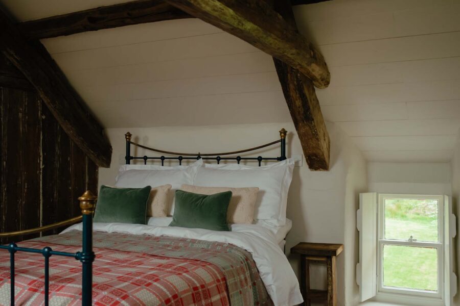 bedroom with wooden beams overhead and iron cast bed with green velvet cushions and a red tartan bedspread