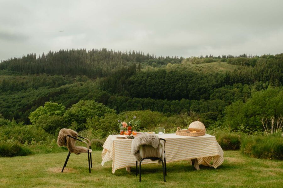 outdoor dining set up in countryside with sheepskins hanging over chairs and a white tablecloth on table
