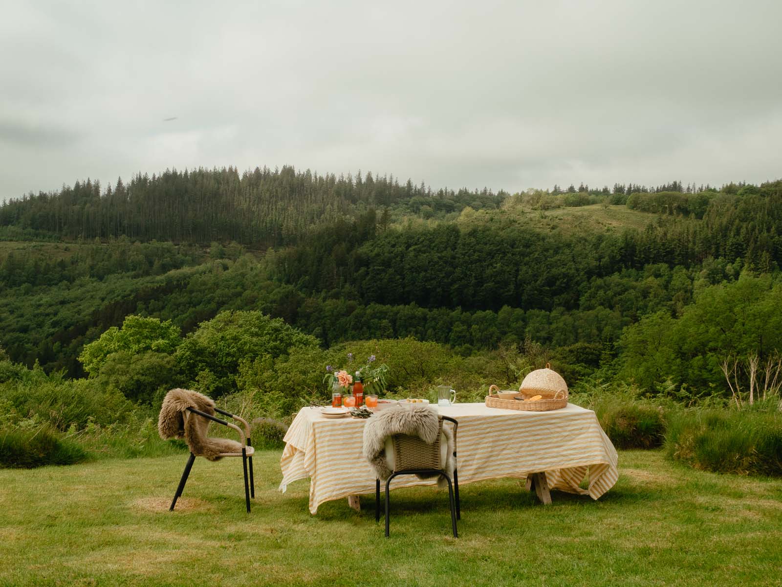 outdoor dining set up in countryside with sheepskins hanging over chairs and a white tablecloth on table