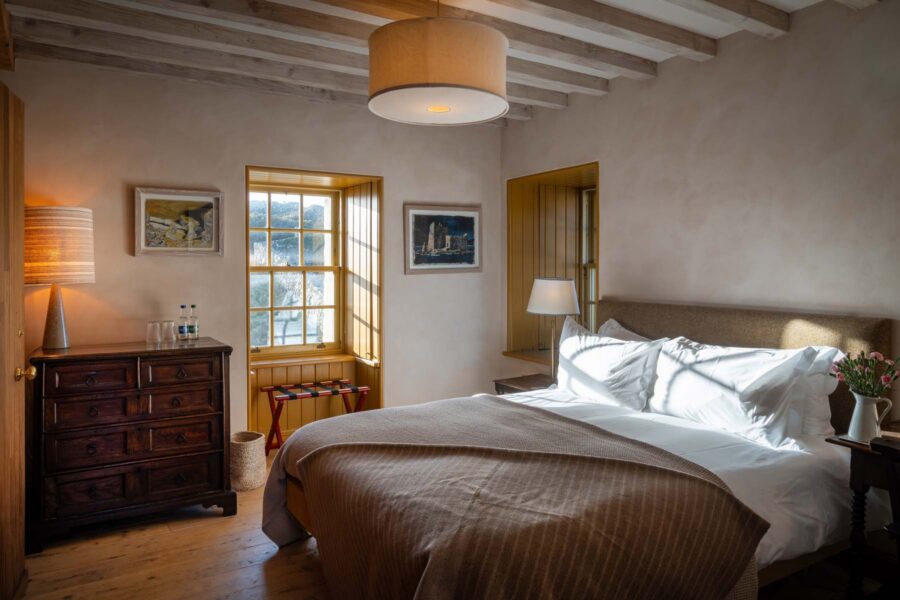 stylish bedroom with high ceiling, wooden beams, and the light flooding in a yellow-hued window